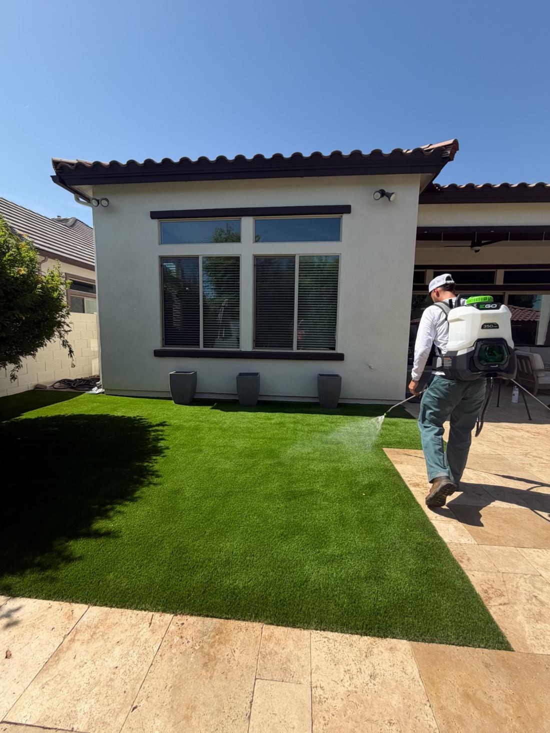 TurfHealth technician applying a low-pressure hydrogen peroxide turf treatment with a backpack sprayer at a Phoenix-area home